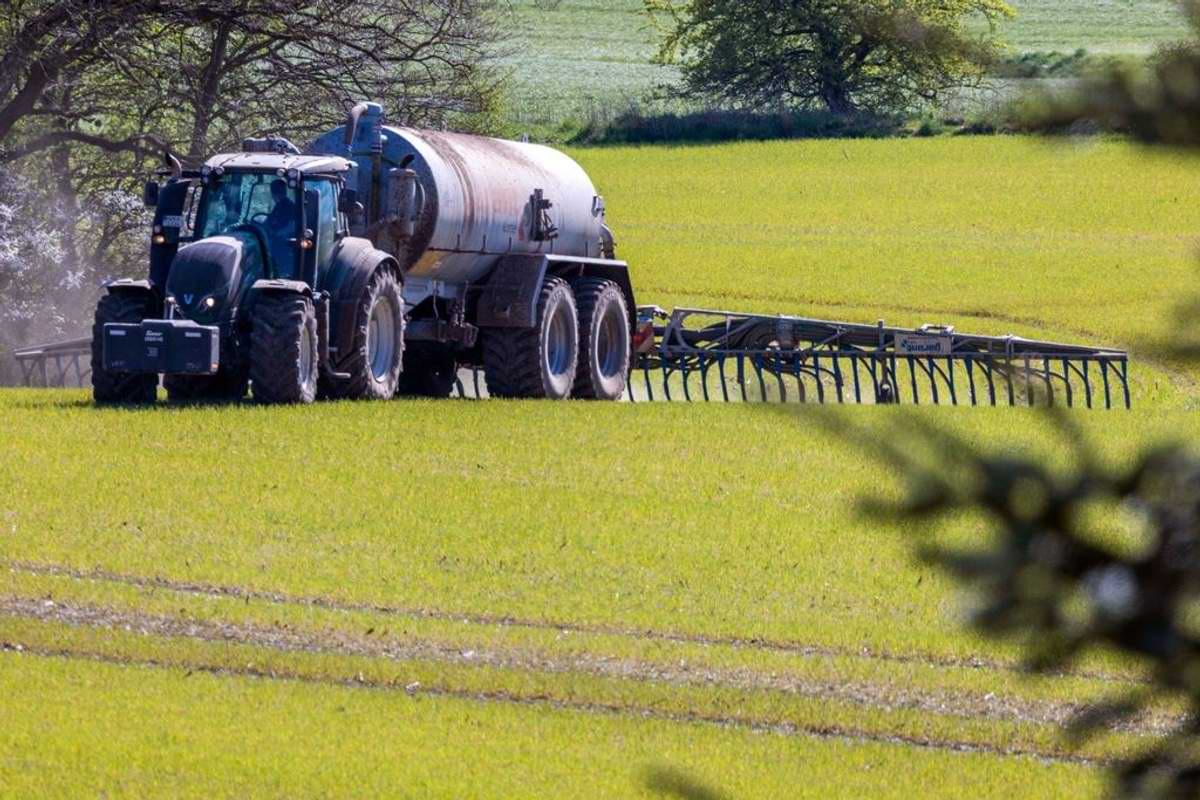 Archivbild Ein Traktor zieht einen Tankwagen über ein Feld und verteilt Gülle im Boden.jpeg