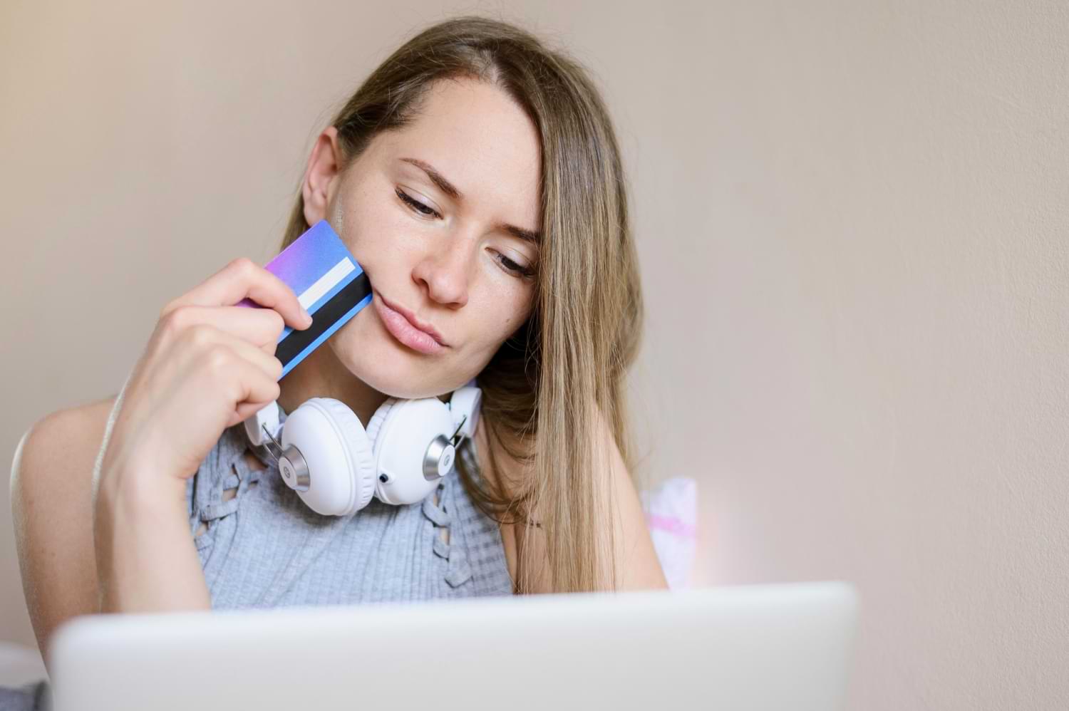 frau mit kopfhörern hält bankkarte an kopf und denk nach am laptop.jpg