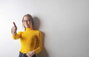 schlaues schönes brillen mädchen mit gelbem pulli macht den daumen hoch.jpg